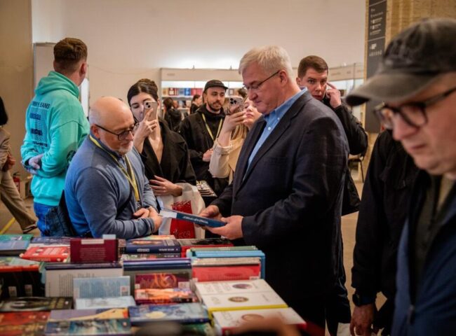 Фото: Видавництво Фоліо. Джерело: https://folio.com.ua/galleries/vidavnictvo-folio-na-knizhkovomu-arsenali-2026 . Умови: https://folio.com.ua/pages/rules . Книжковий Арсенал, 2026; репортажне фото події видавництва. Зустріч відвідувачів зі співробітниками Фоліо біля книжкового стенда на Книжковому Арсеналі